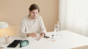 Young man tests his blood sugar using a glucometer while sitting at a table indoors.